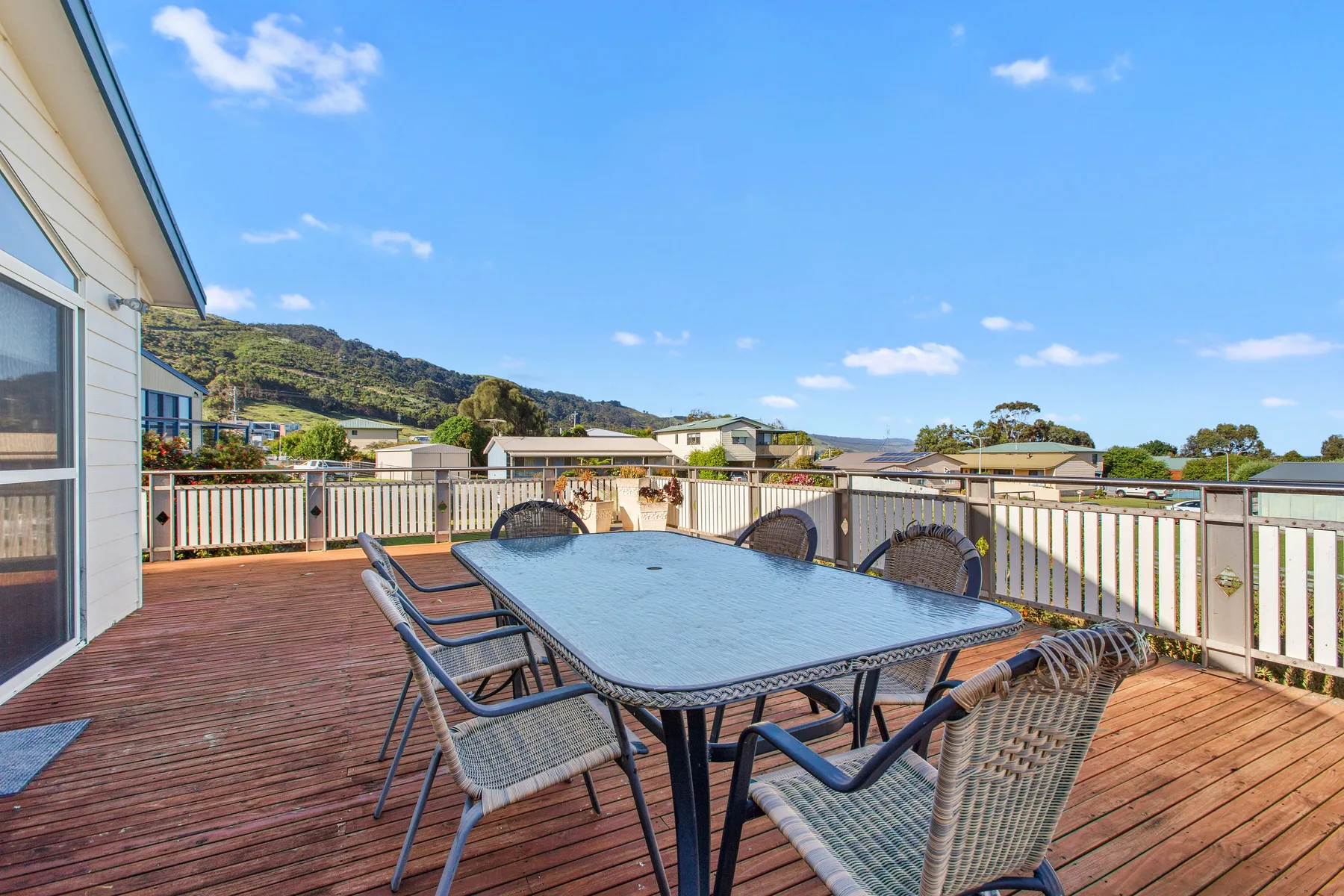Una terraza exterior tiene una mesa de comedor y sillas junto a una barandilla.
