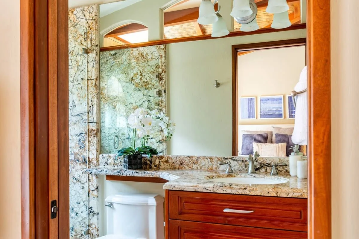 A bathroom vanity with a wide mirror and a marble-patterned wall.