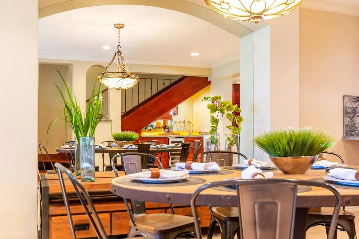 A dining area with a long wooden table, metal seating, and hanging lights.