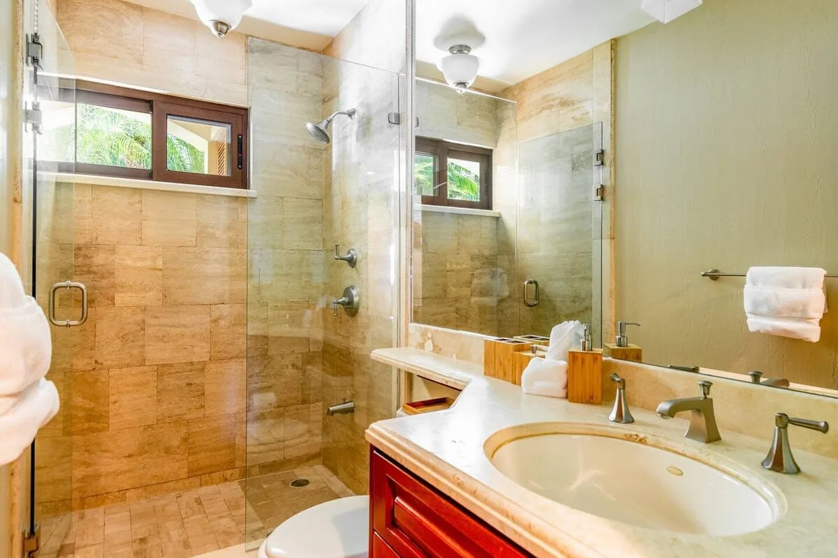 A bathroom with a glass shower, a sink, and a small window.