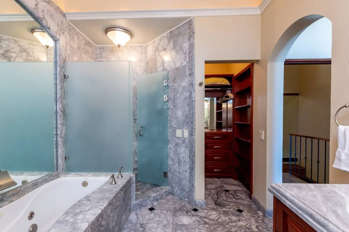 A bathroom with a bathtub, glass shower enclosure, and marble-patterned surfaces.