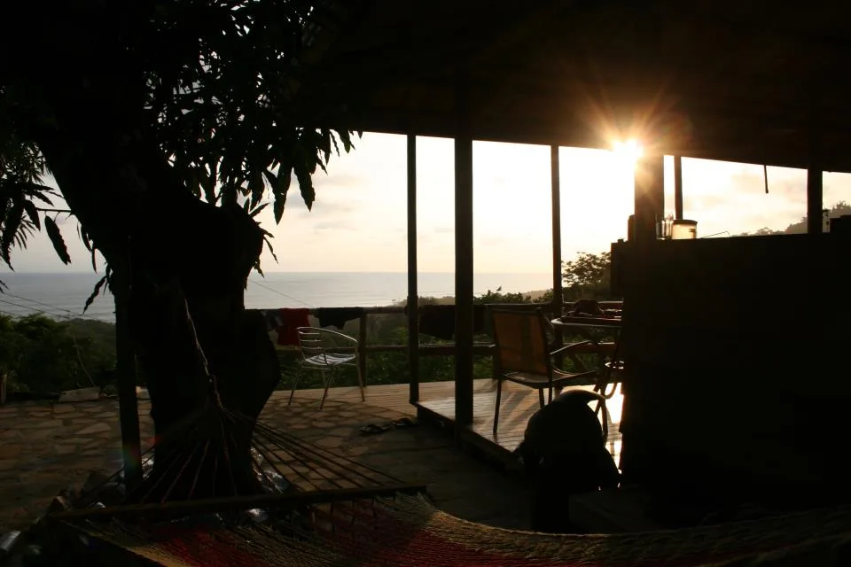 Un patio cubierto junto al mar con asientos al aire libre mira hacia el océano al atardecer.