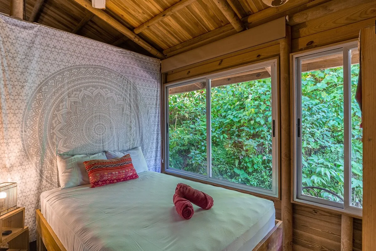 Un dormitorio con una cama bajo grandes ventanas que dan a una frondosa vegetación.