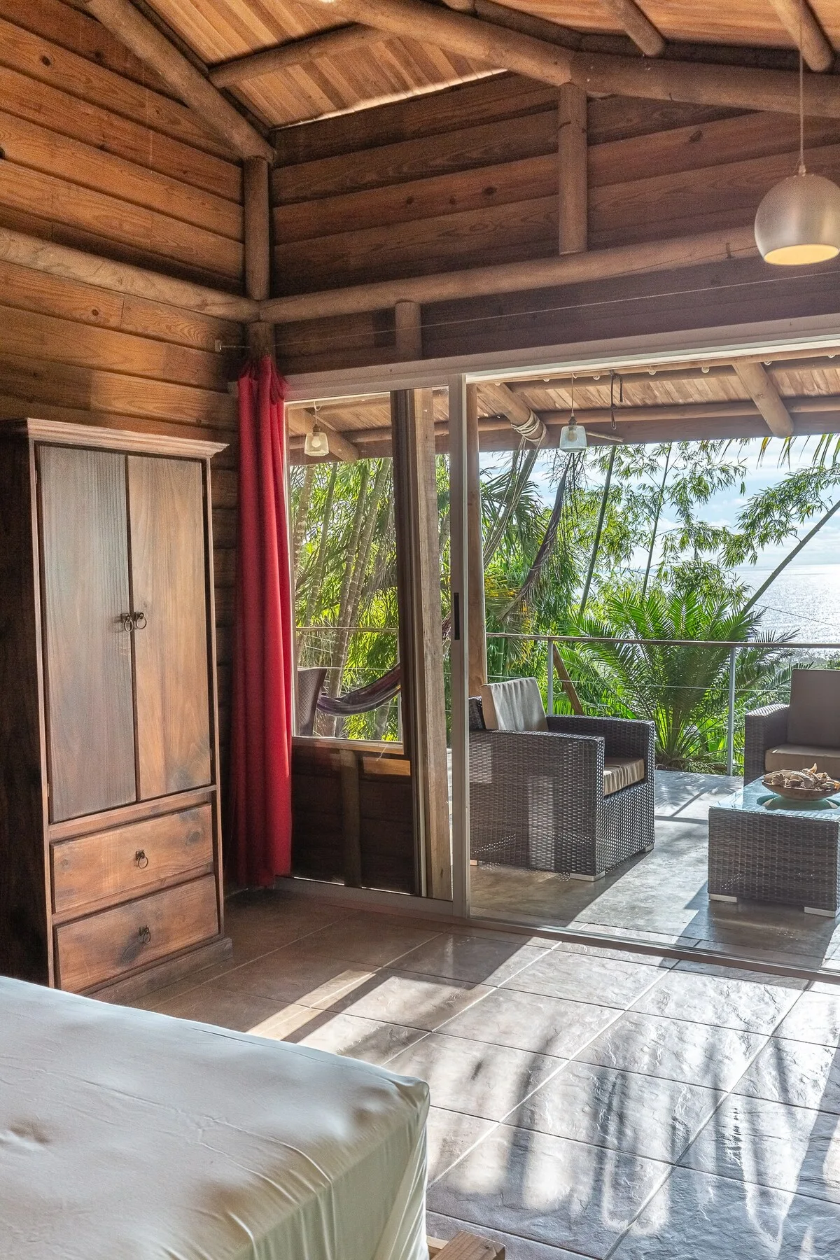 Un dormitorio se abre a un patio cubierto con asientos y vistas a la vegetación y al agua.