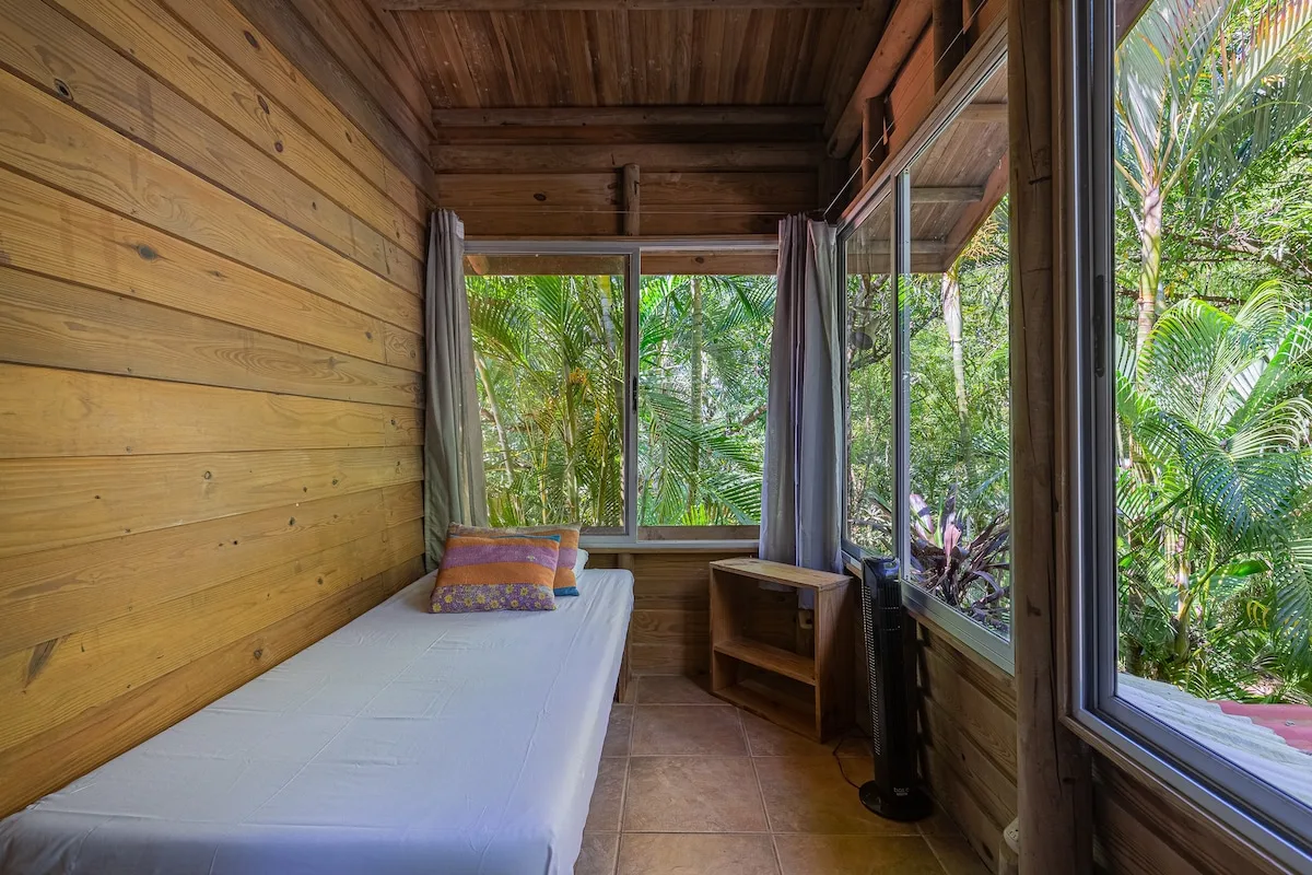 Un dormitorio con una cama junto a grandes ventanas que dan a una frondosa vegetación.