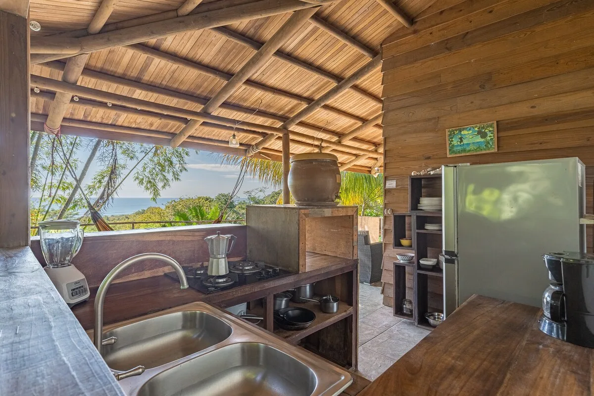 Una cocina exterior cubierta con fregadero, encimera y vistas abiertas a la vegetación.