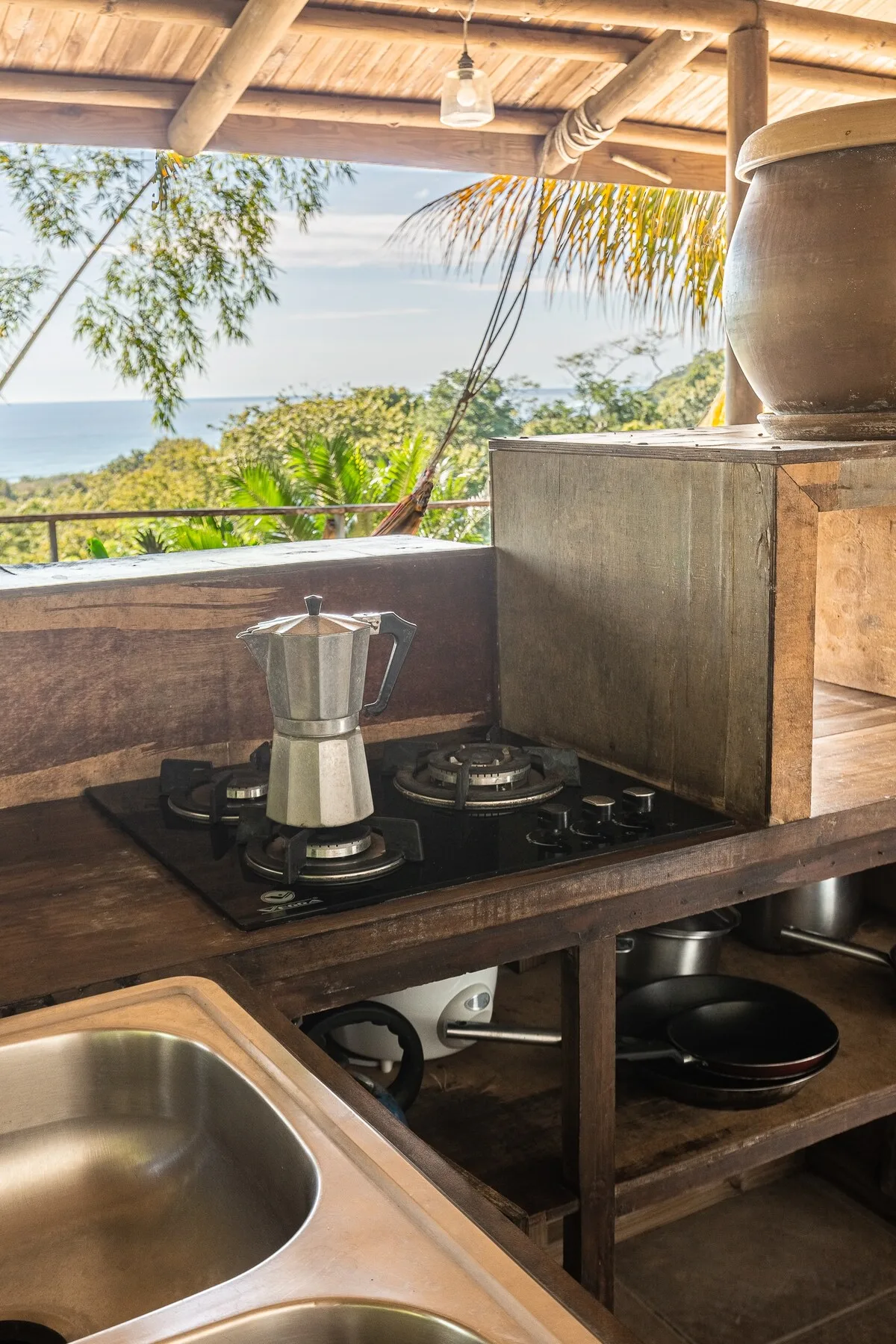 Una encimera de cocina al aire libre con fogón, fregadero y vistas a la vegetación y al mar.
