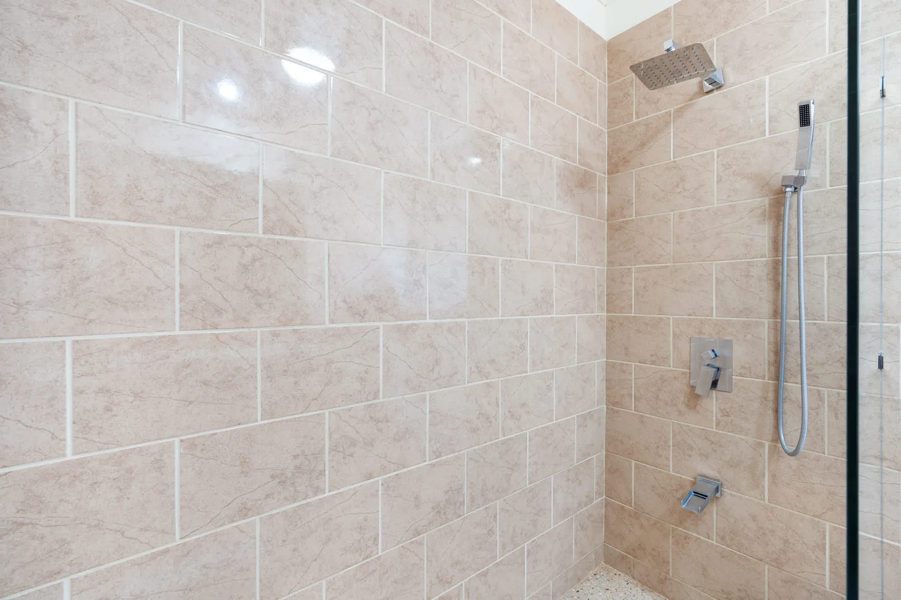 A tiled shower with a wall-mounted showerhead and handheld sprayer.