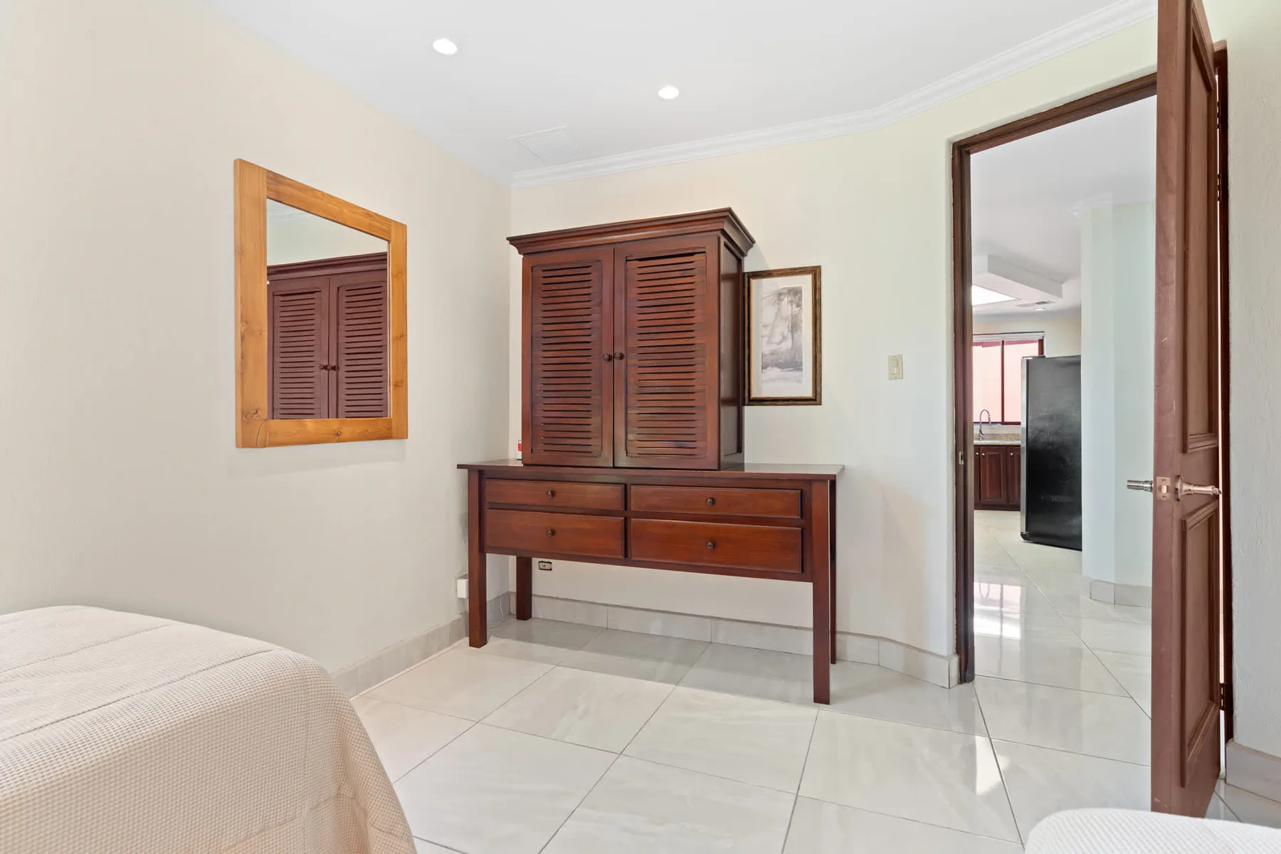 A bright bedroom with a wooden dresser and a doorway opening to another room.