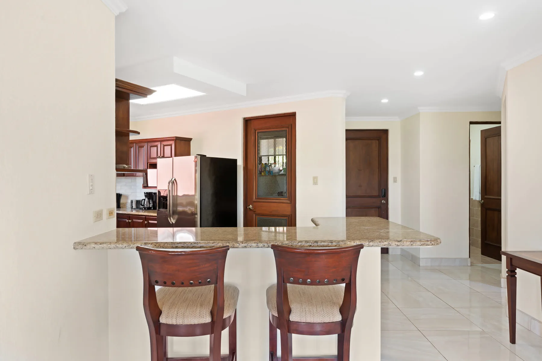 A bright kitchen and dining area with a stone counter and two seats.