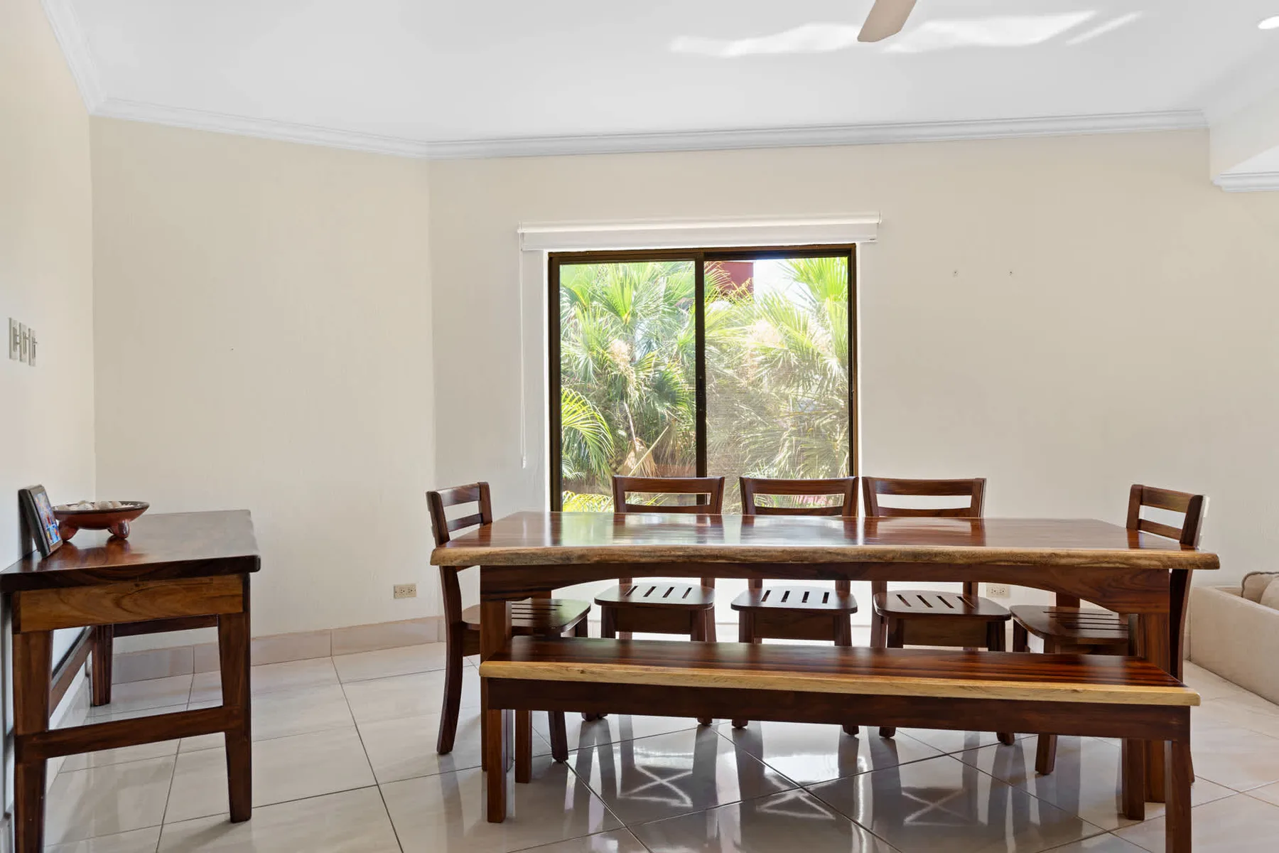 A dining area with a long wooden table and seating beside a large window.