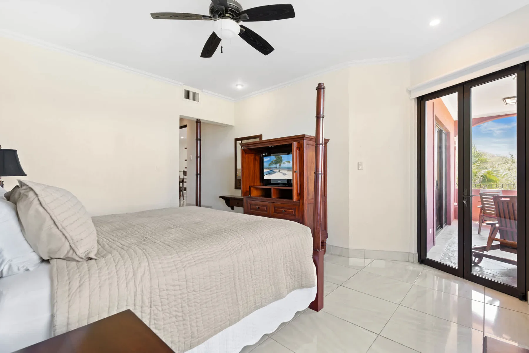 A bedroom with a bed, wooden entertainment unit, and glass doors opening onto a patio.