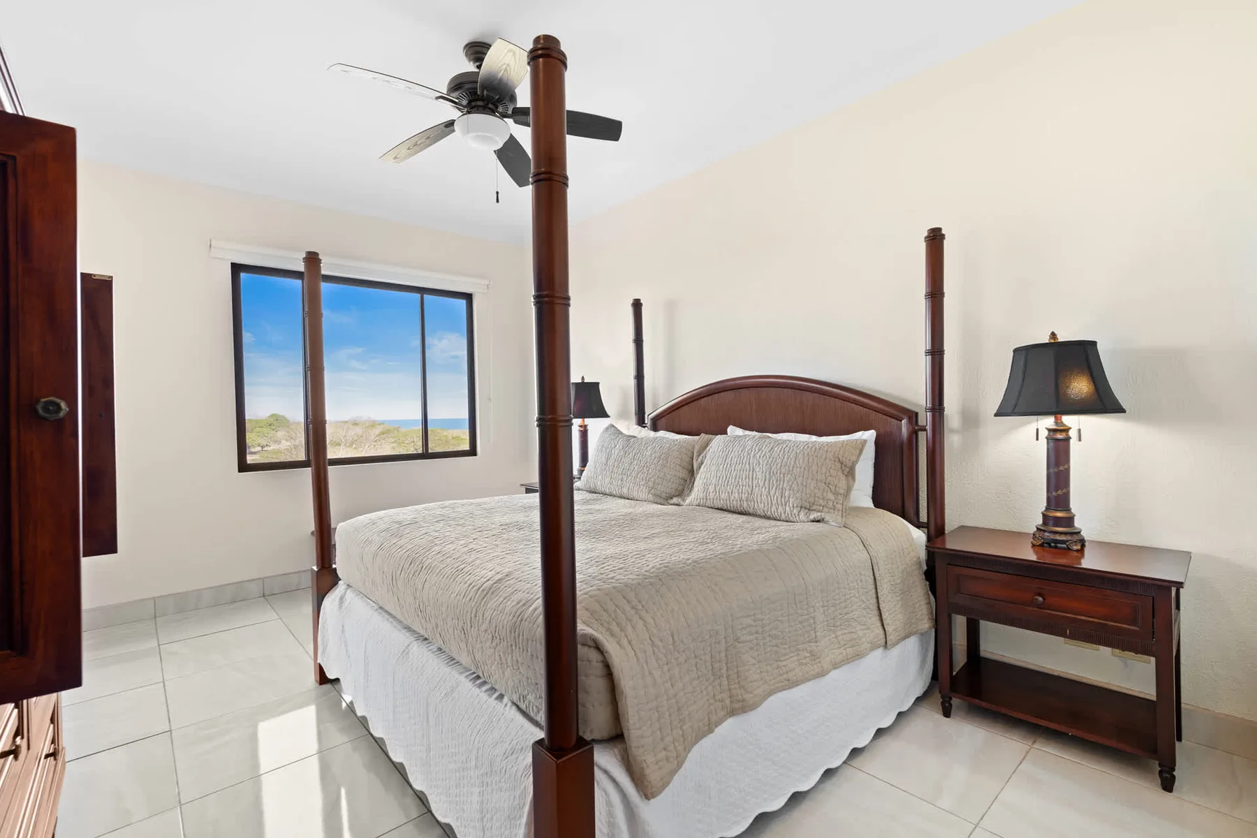 A bedroom with a four-poster bed, a window, and a bedside table.