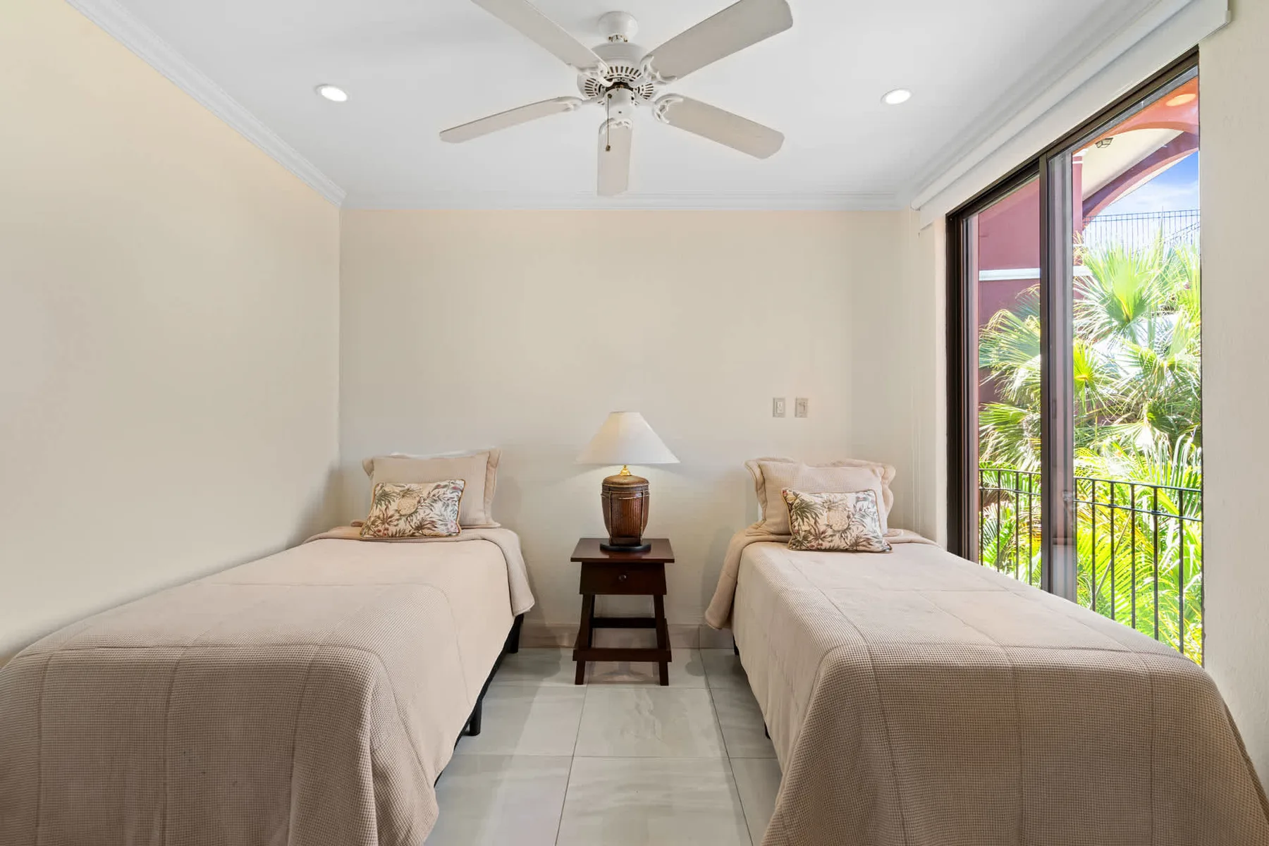 A bright bedroom with two beds beside large glass doors opening to greenery.