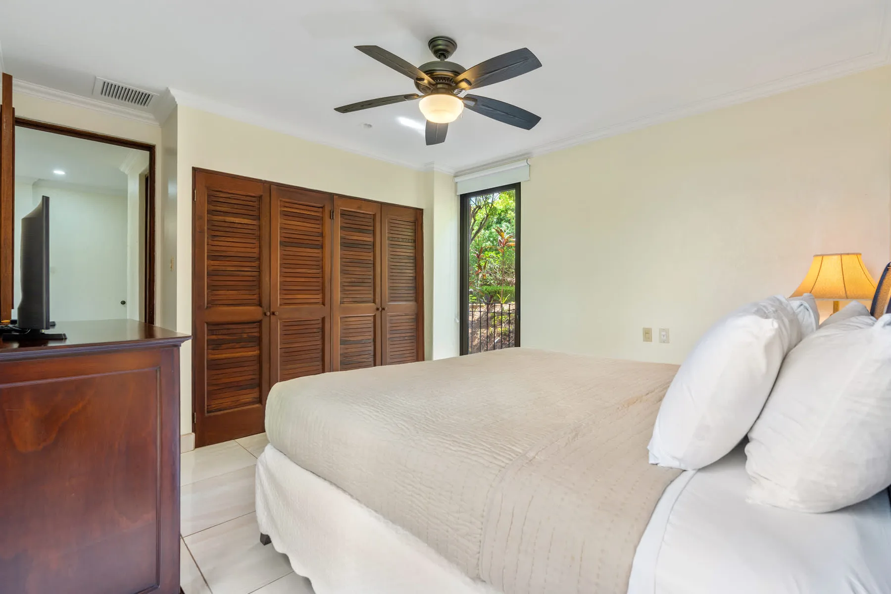 A bedroom with a large bed, wooden louvered doors, and a ceiling fan.