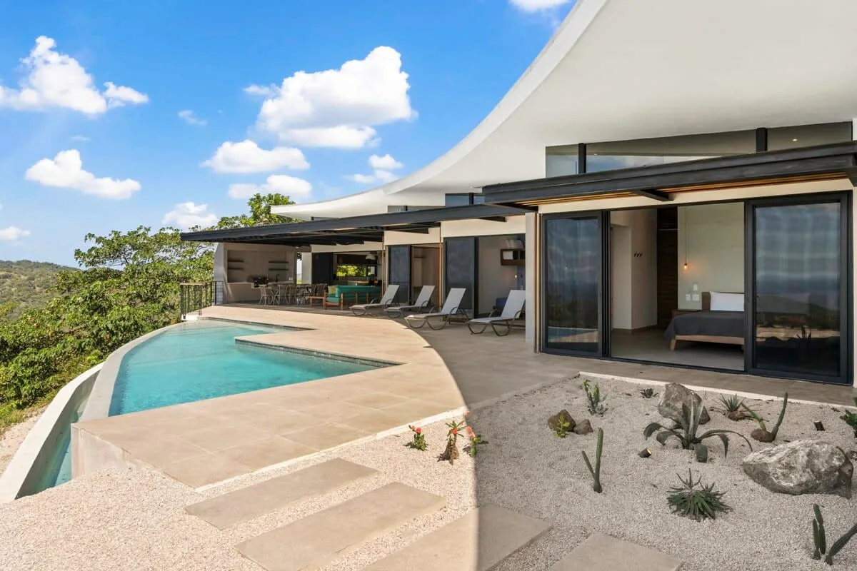 A curved outdoor pool beside a modern house and landscaped patio.