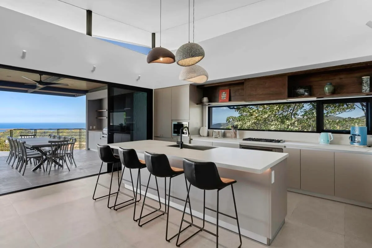 A modern kitchen with a large island and an outdoor dining area beyond the open doors.