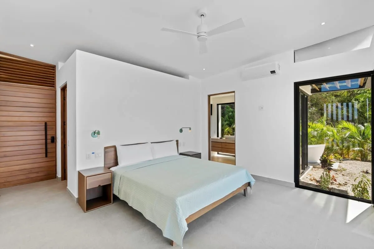 A bright bedroom with a neatly made bed and glass doors opening onto greenery.