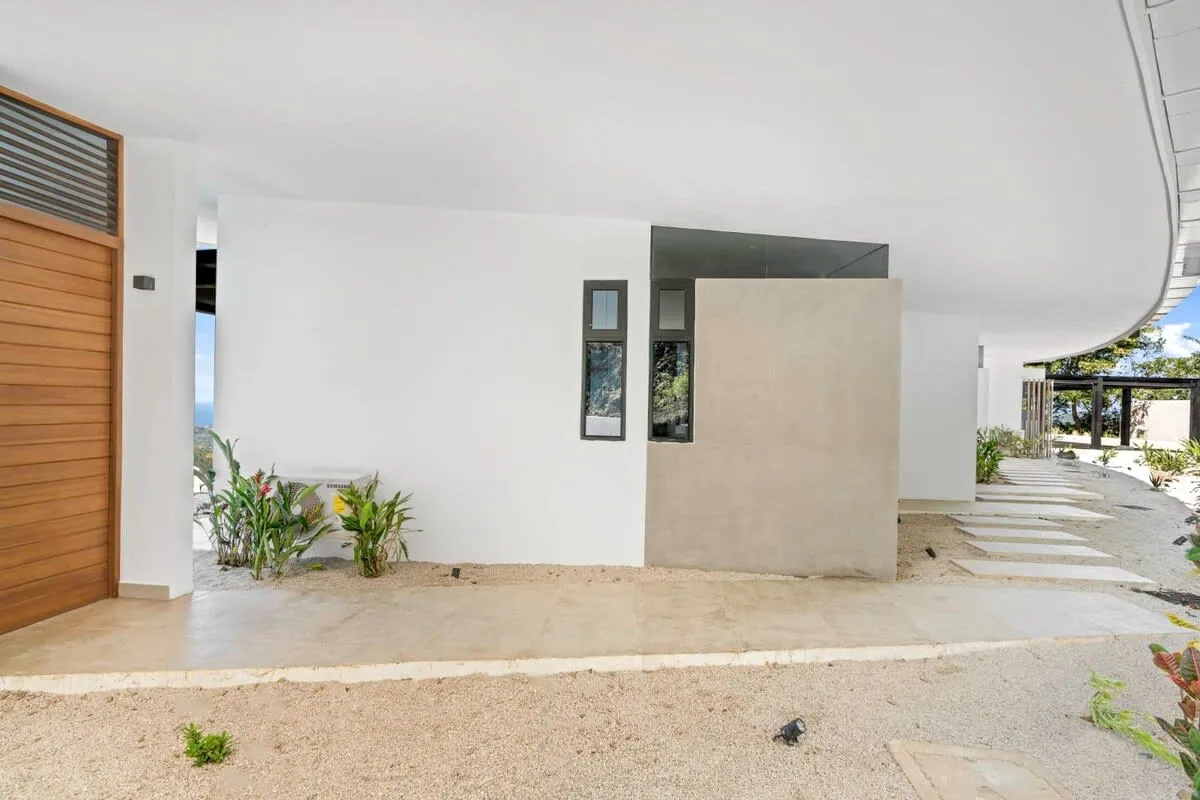 A modern building entrance opens onto a covered walkway beside a landscaped garden.