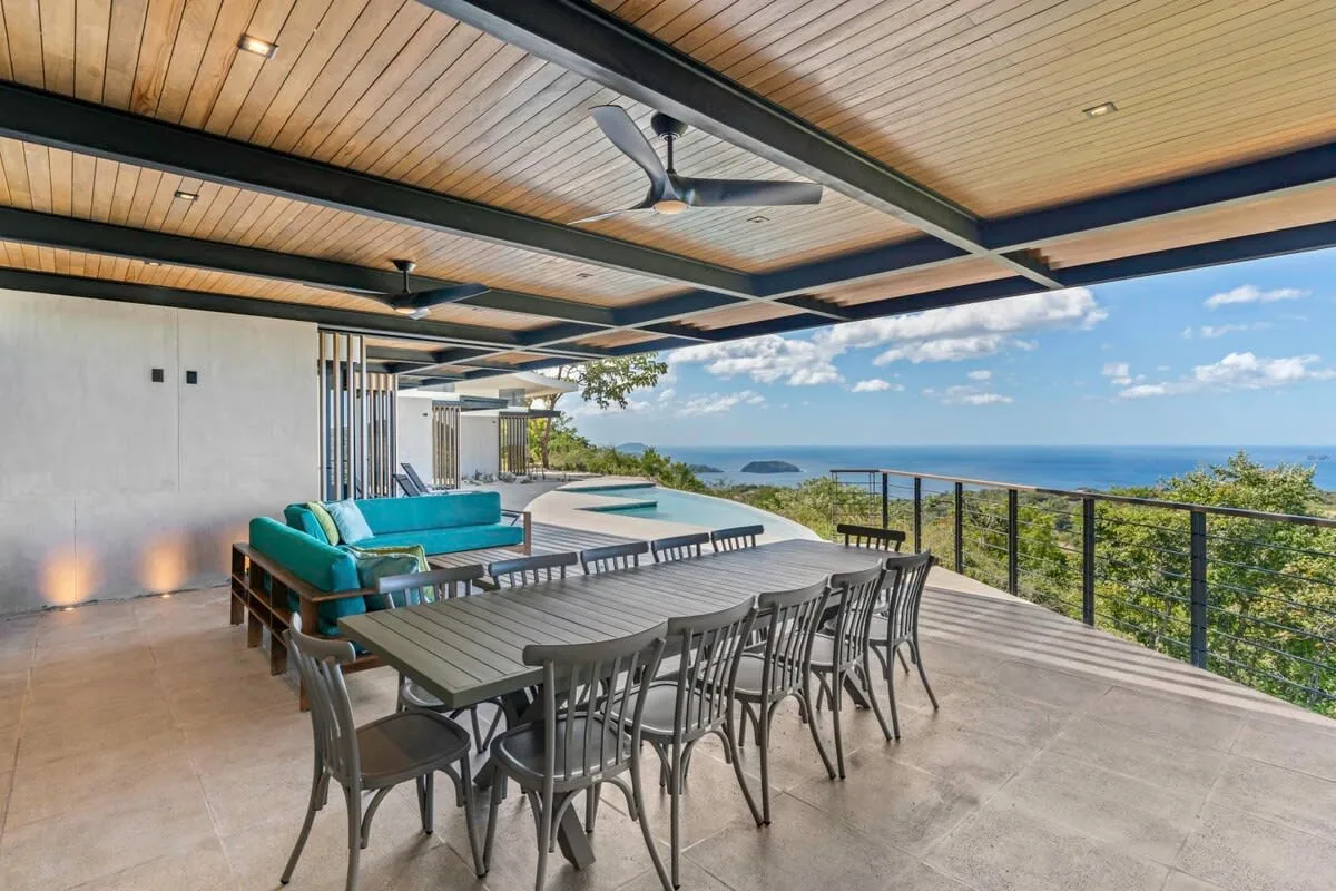An outdoor dining area with a long table overlooks the ocean.