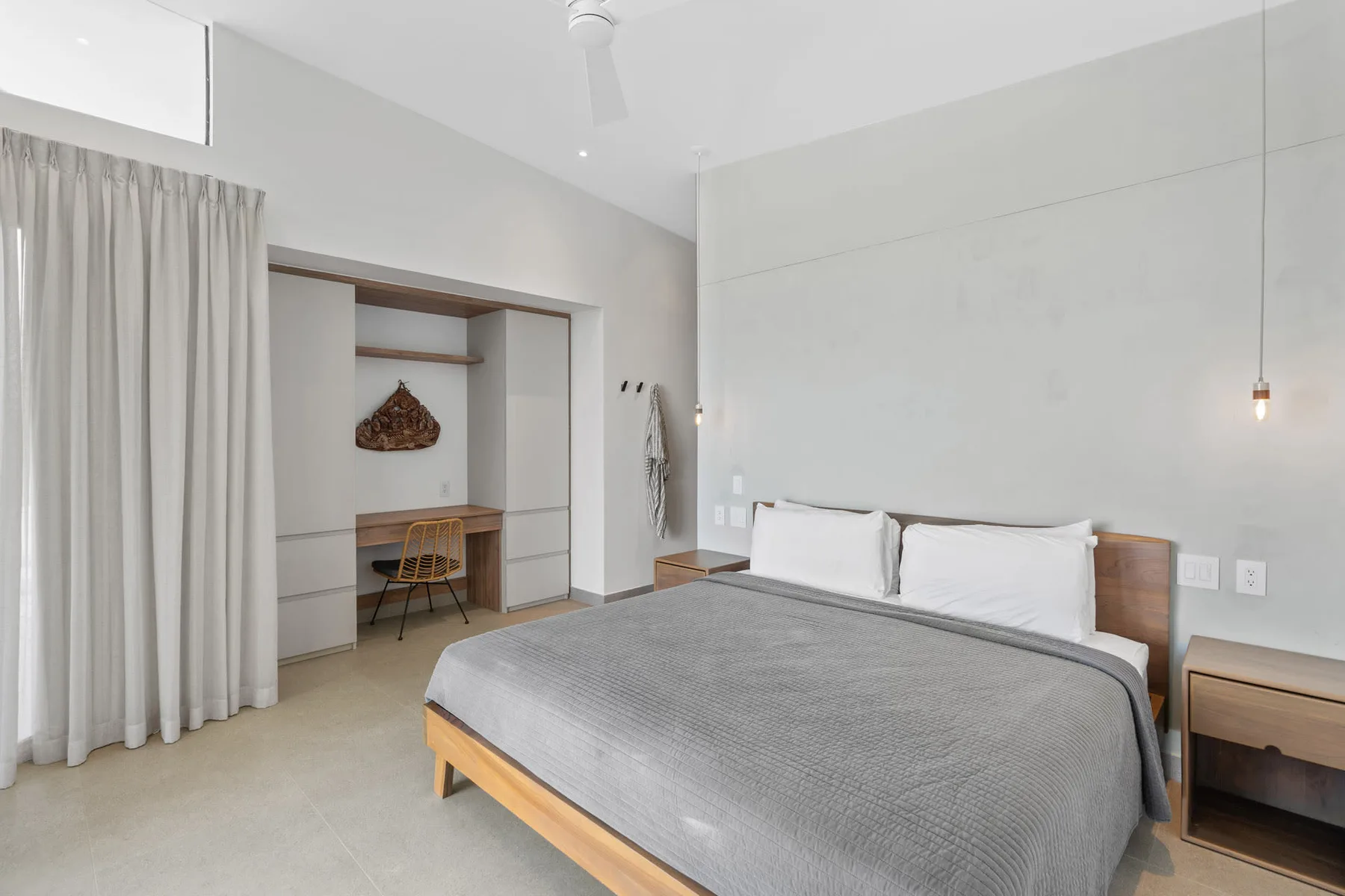 A bright bedroom with a bed, built-in shelving, and floor-length curtains.