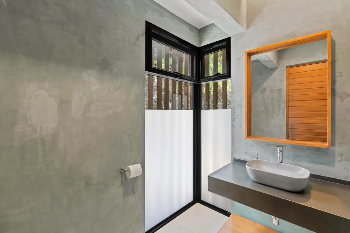 A modern bathroom with a vessel sink, wall mirror, and frosted lower window panes.