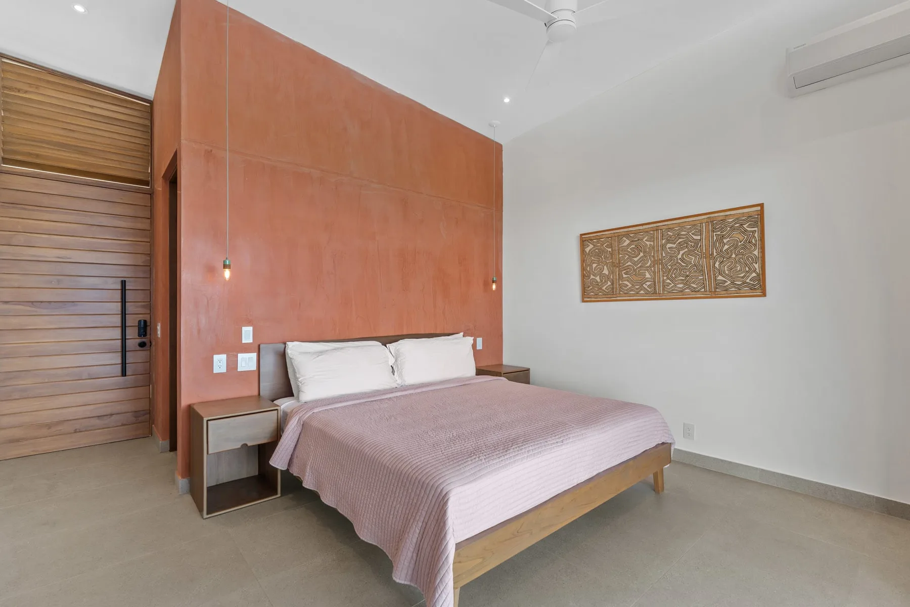 A bedroom with a bed beneath a terracotta-colored accent wall.