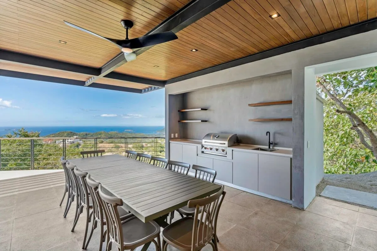 An outdoor dining area with a long table, grill, and ocean view.