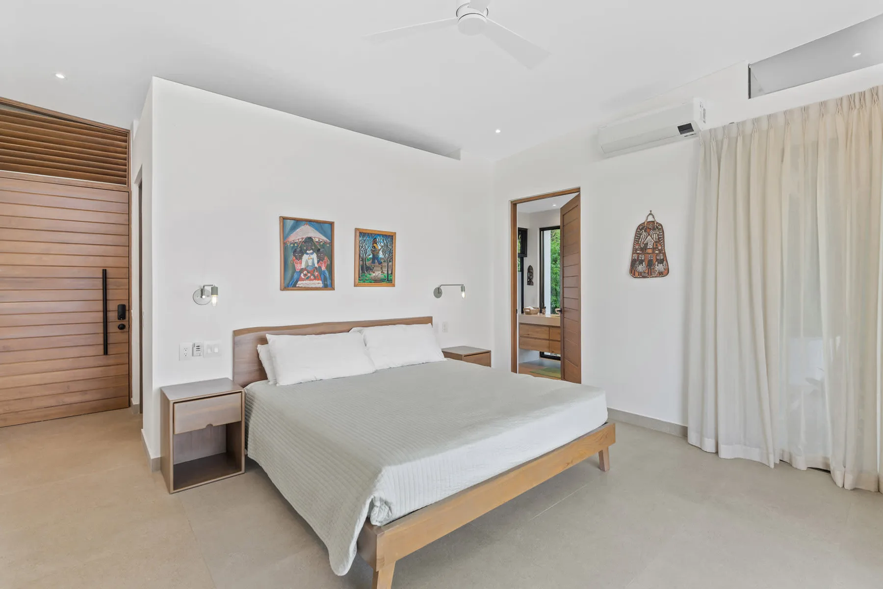 A bedroom with a bed, bedside tables, and light curtains.