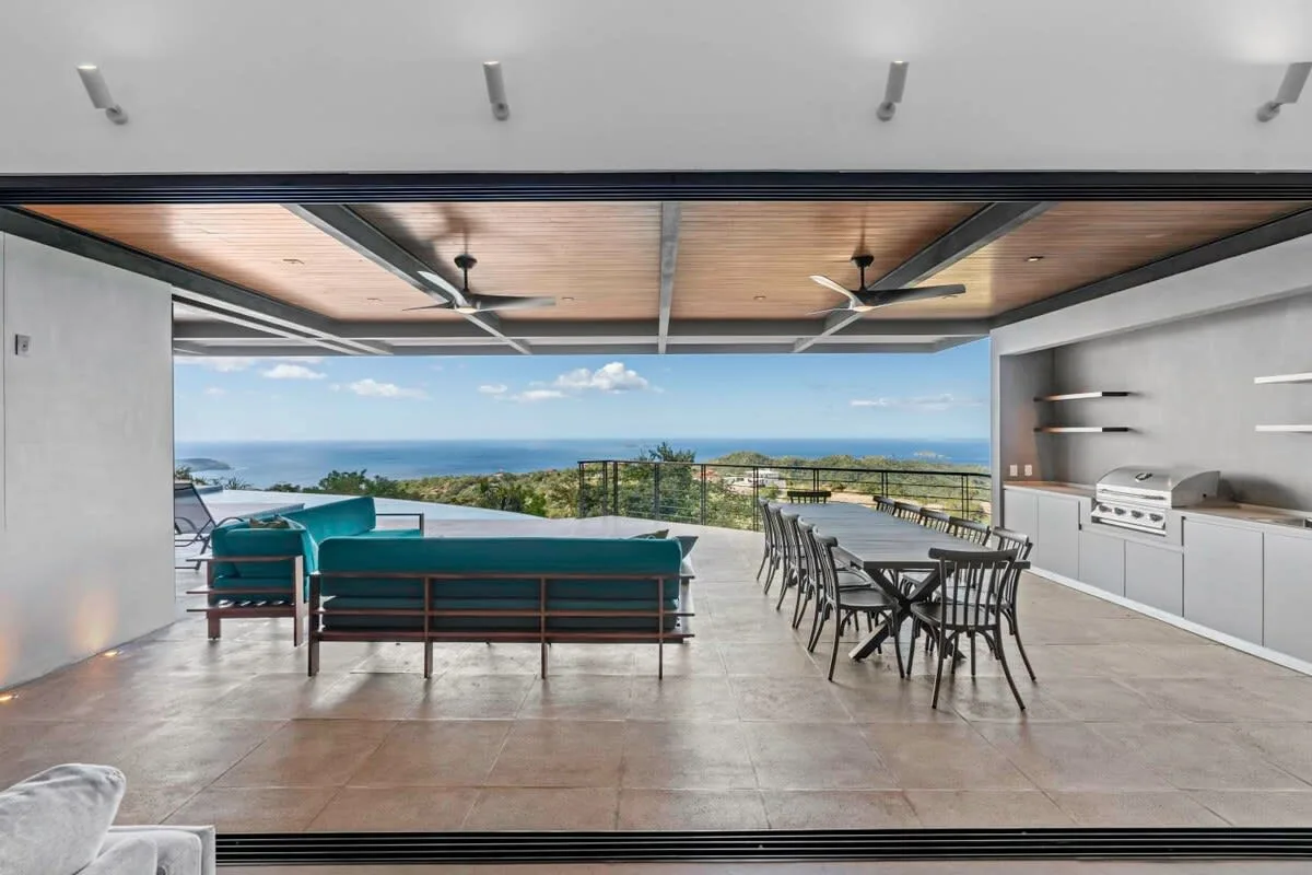 An open-air terrace has lounge seating, a dining table, and a view of the sea.