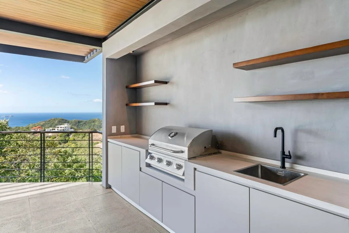 An outdoor kitchen with a built-in grill and sink overlooks the ocean.