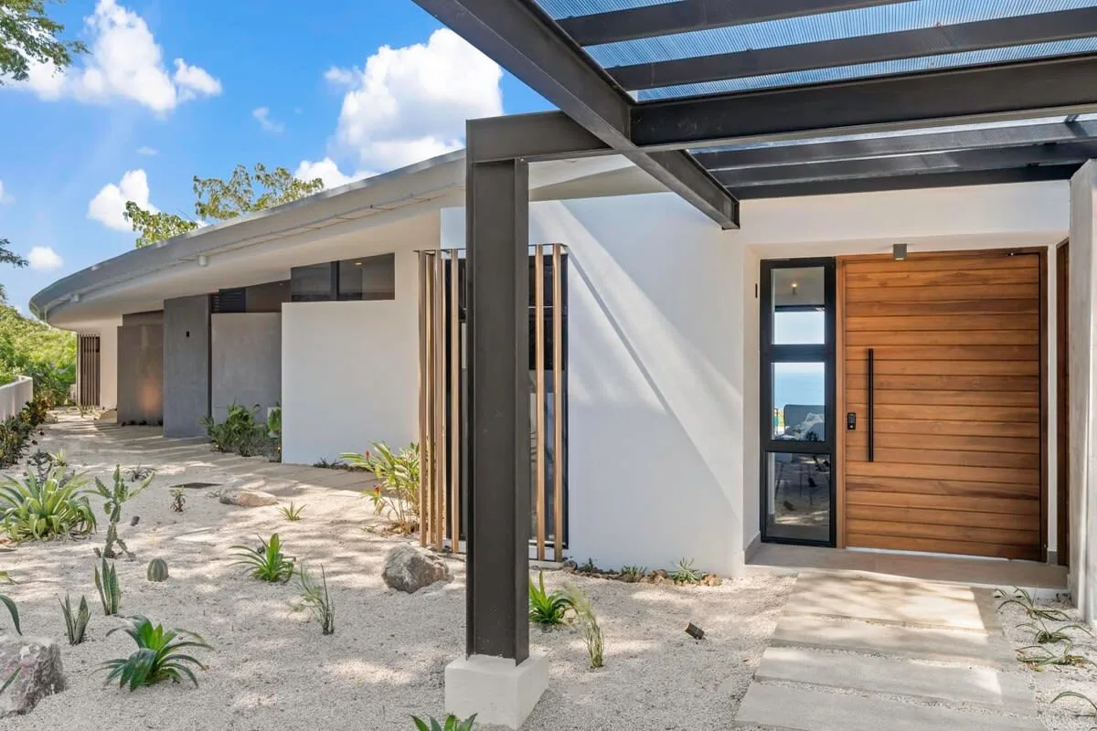 A modern house entrance with a wooden front door and a sandy garden.