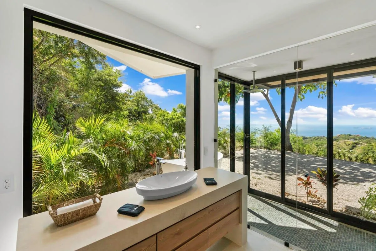 A bright bathroom with a vessel sink and glass doors opening onto a leafy outdoor view.