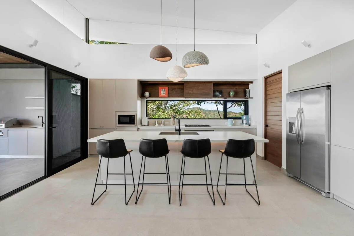 A modern kitchen features a central island with seating and pendant lights.
