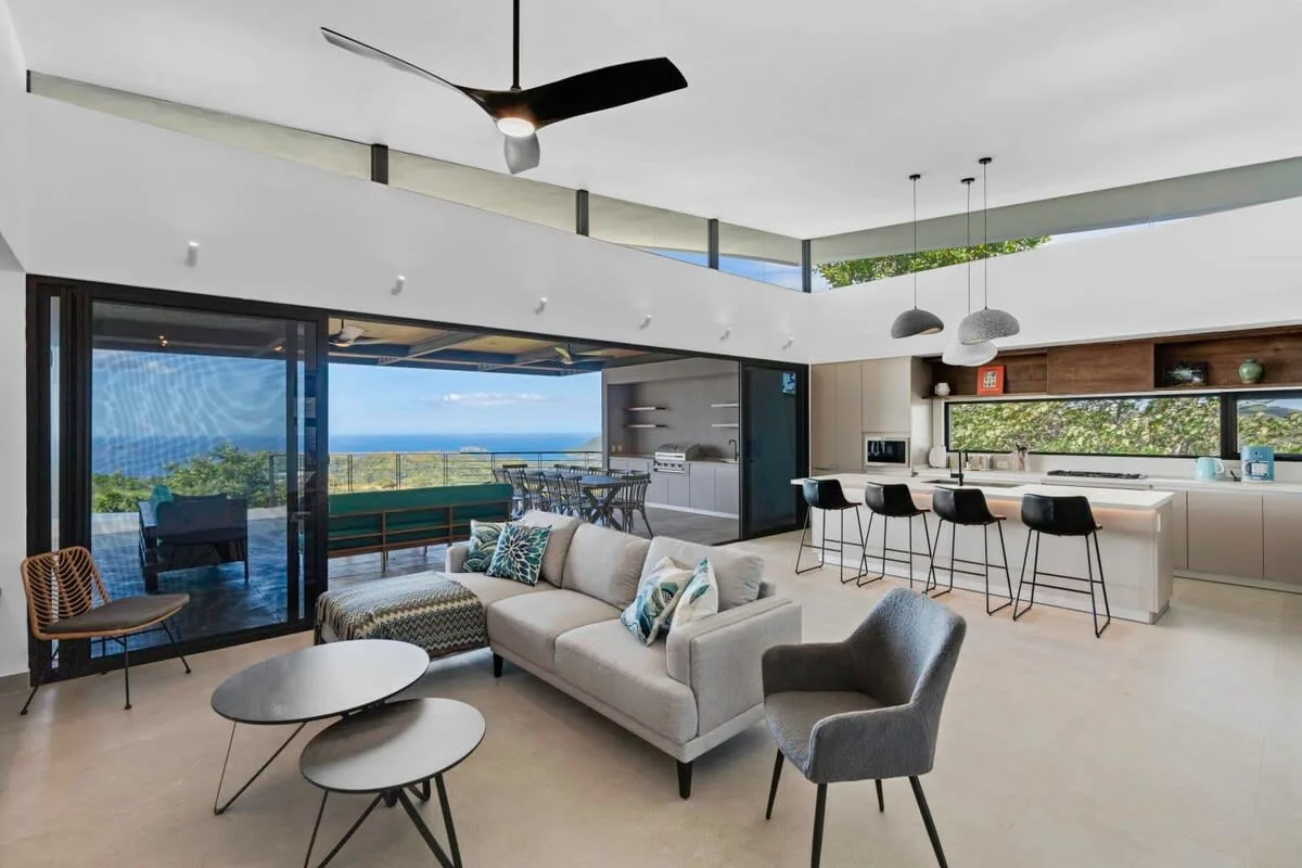 A bright open-plan living room with seating beside a kitchen island and large windows.
