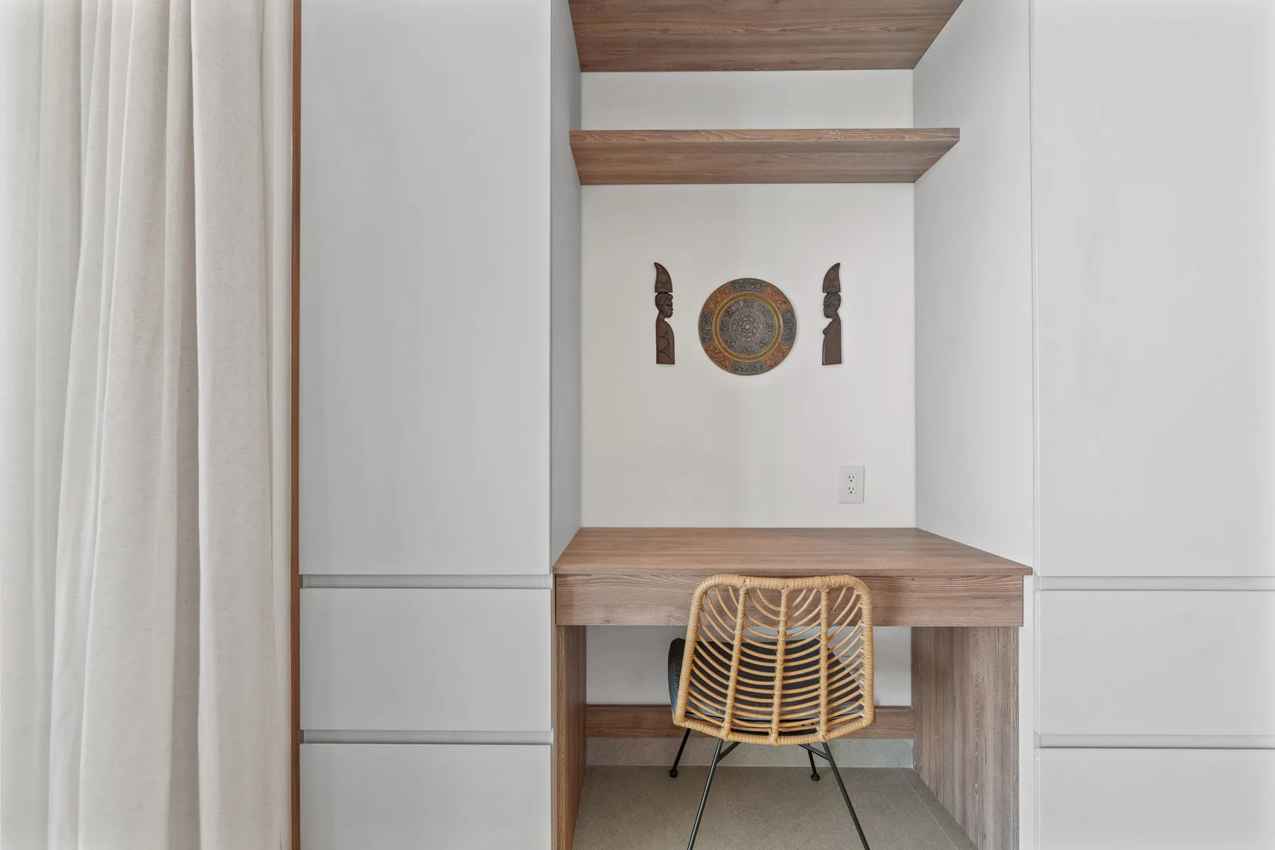 A built-in desk nook with a woven chair and round wall decoration.