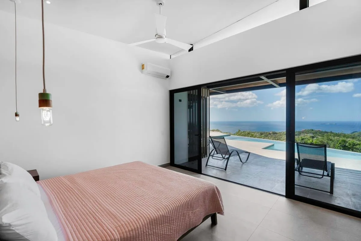 A bedroom opens onto a terrace with seating and a sea view.