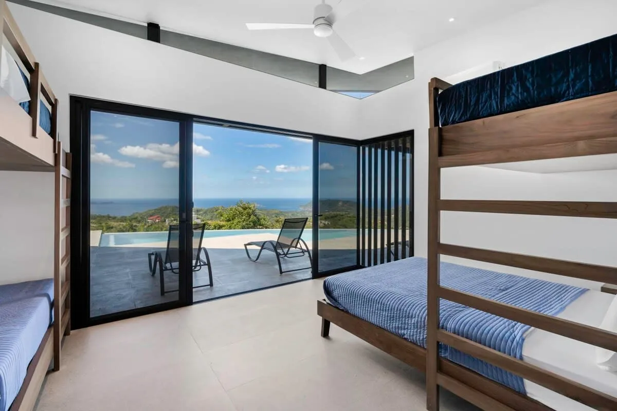A bright bedroom opens onto a patio with a pool and ocean views.