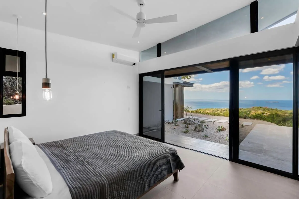 A bright bedroom opens through sliding glass doors to a terrace overlooking the sea.