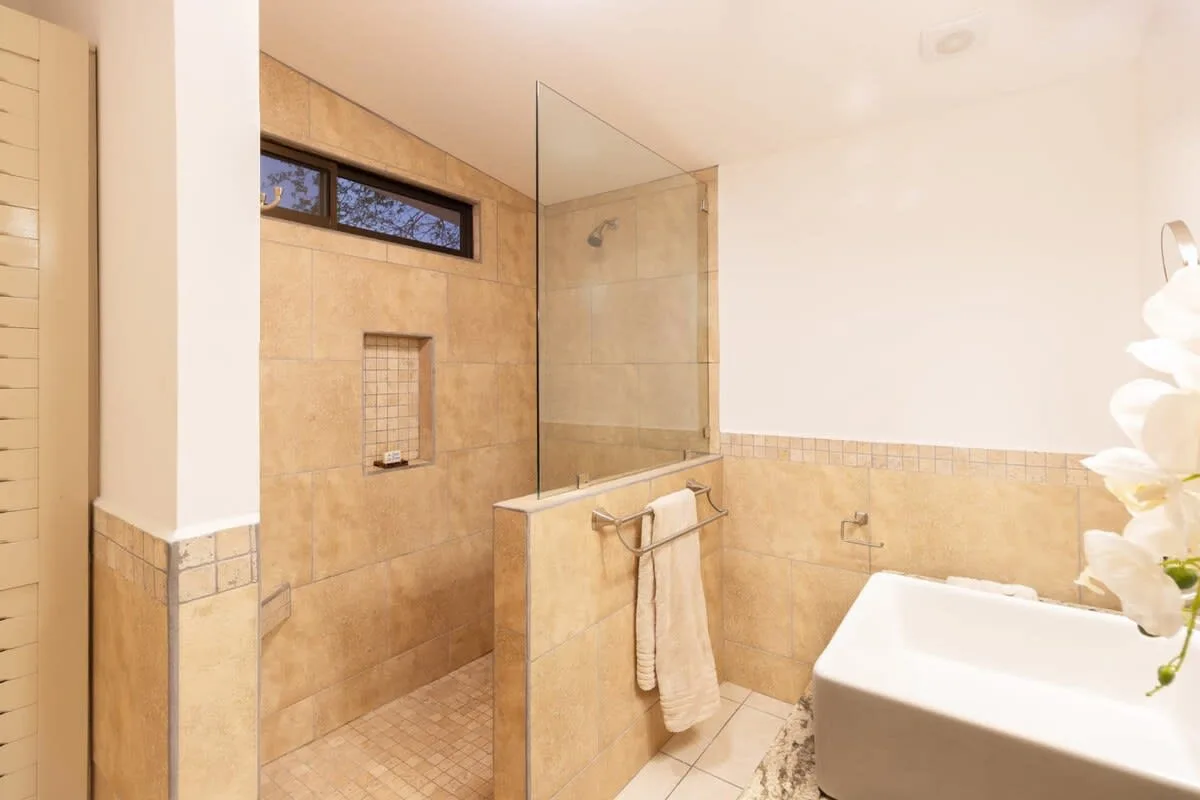 A tiled bathroom features a glass shower screen and a bathtub.
