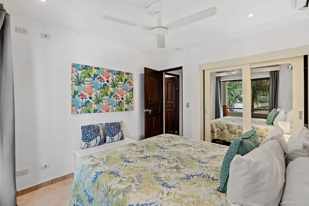 A bedroom with a patterned bedspread, wall art, and an open doorway.