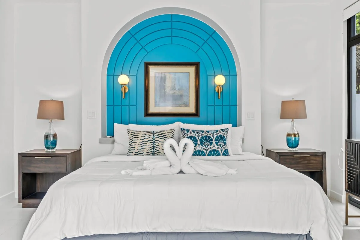 A bedroom with a neatly made bed, patterned pillows, and a bright blue arched wall feature.