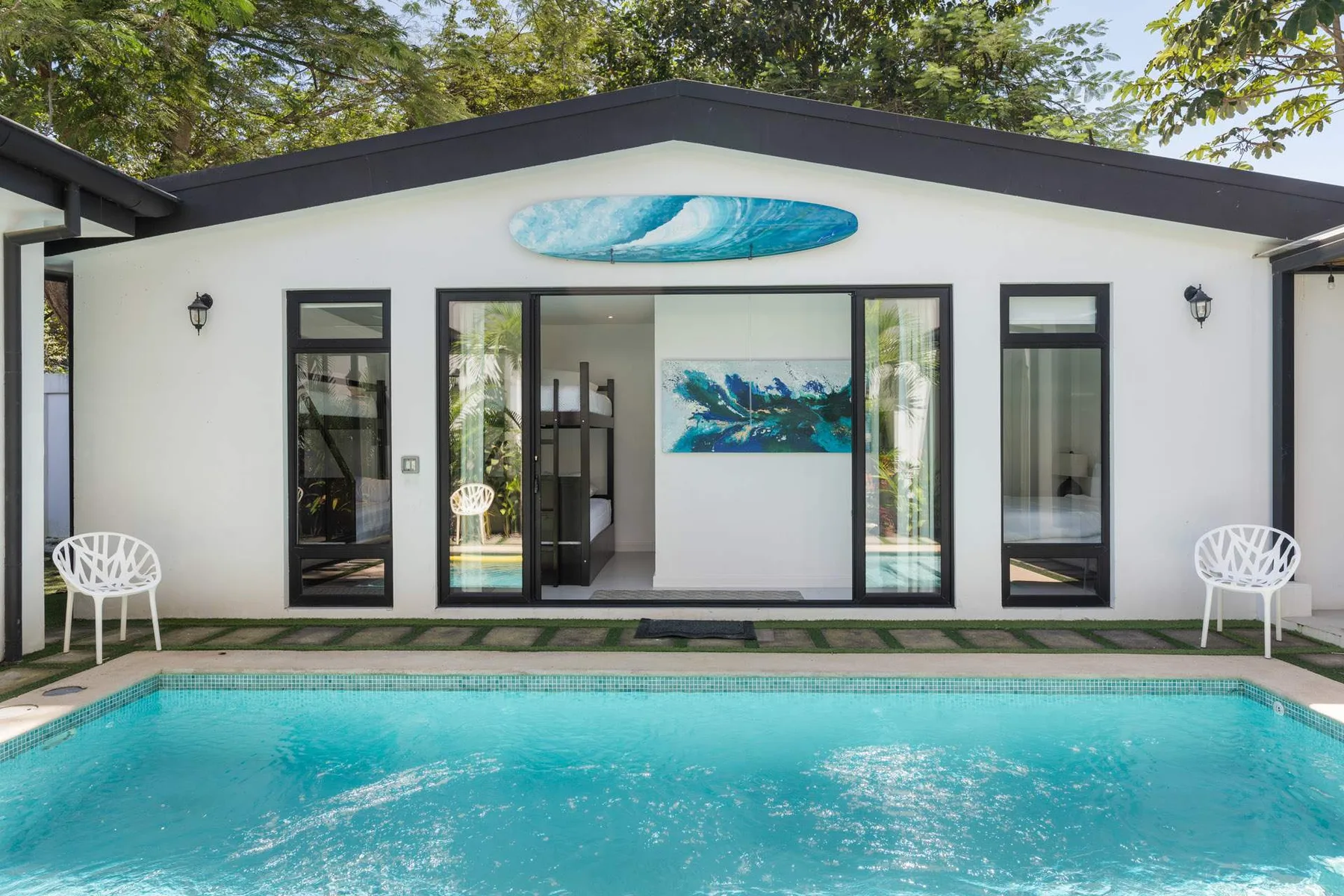 A swimming pool sits in front of a modern white building with glass doors.
