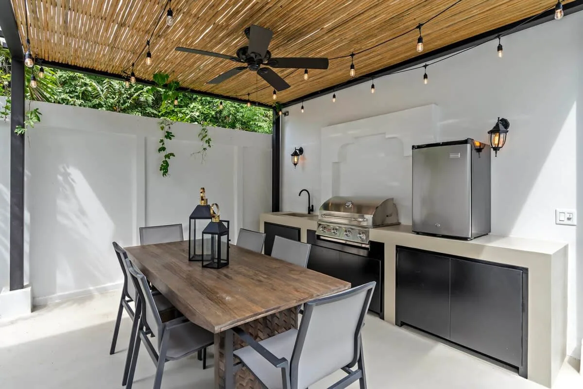 An outdoor dining area with a wooden table beside a built-in grill and refrigerator.