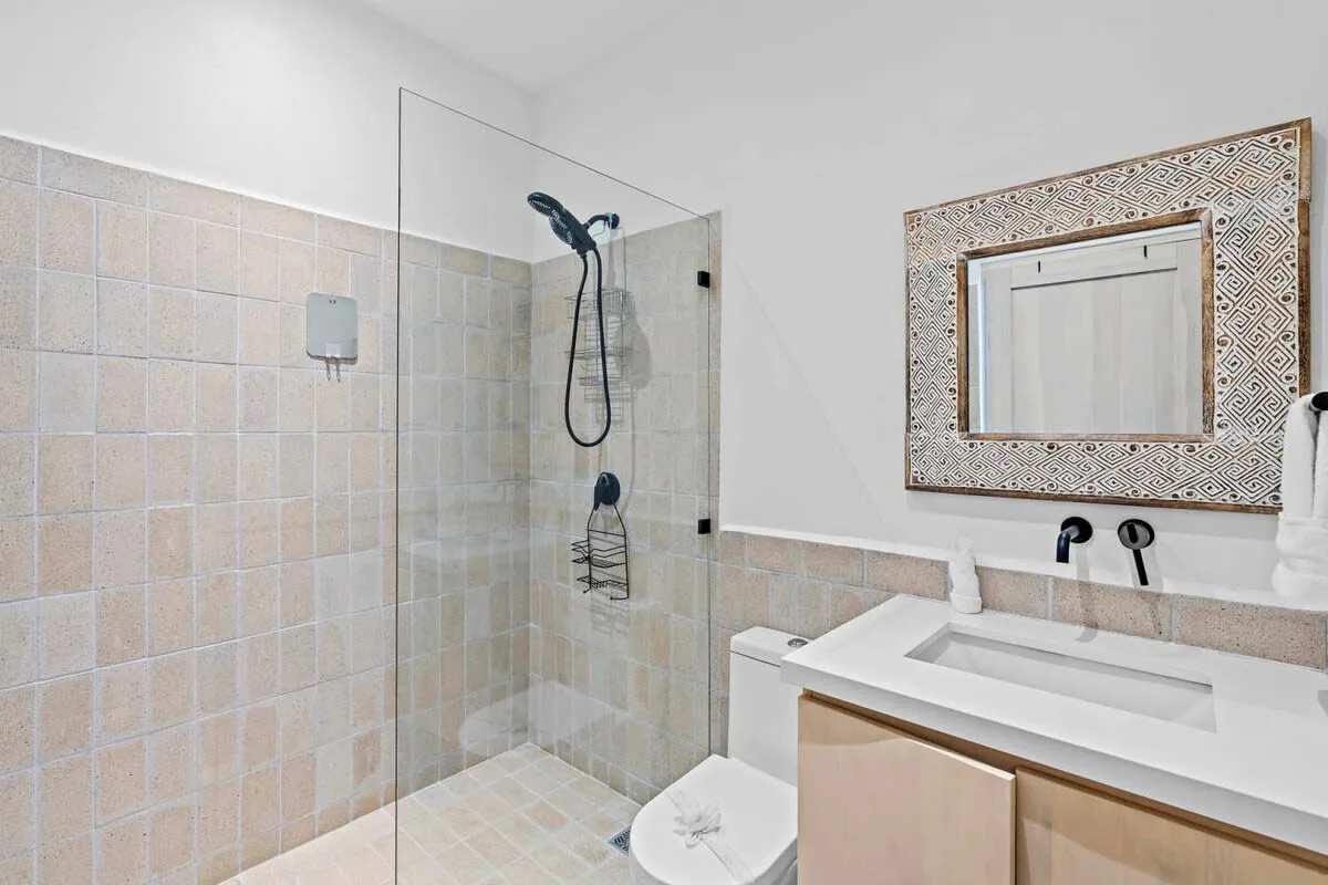 A bathroom with a glass shower, toilet, and sink beneath a framed mirror.