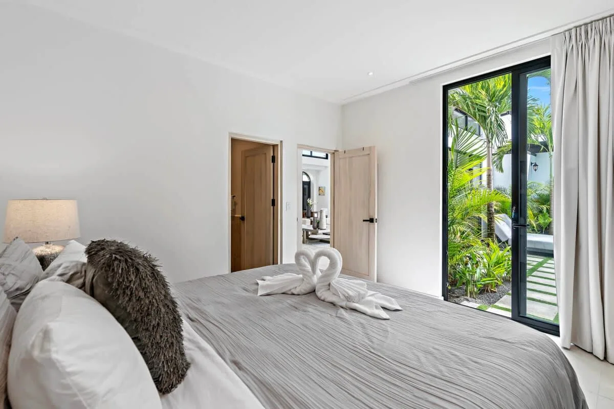 A bright bedroom with a neatly made bed and glass doors opening to greenery.