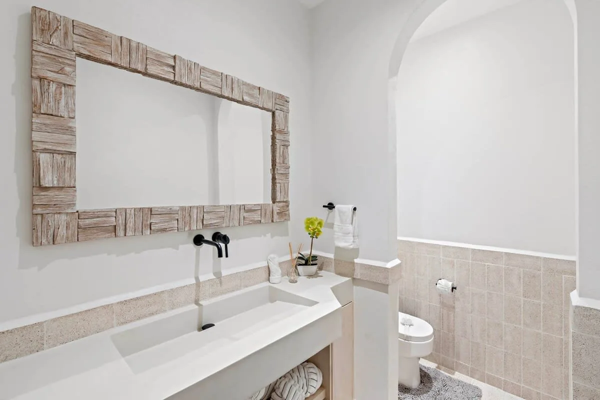 A bright bathroom with a long sink beneath a rustic framed mirror.