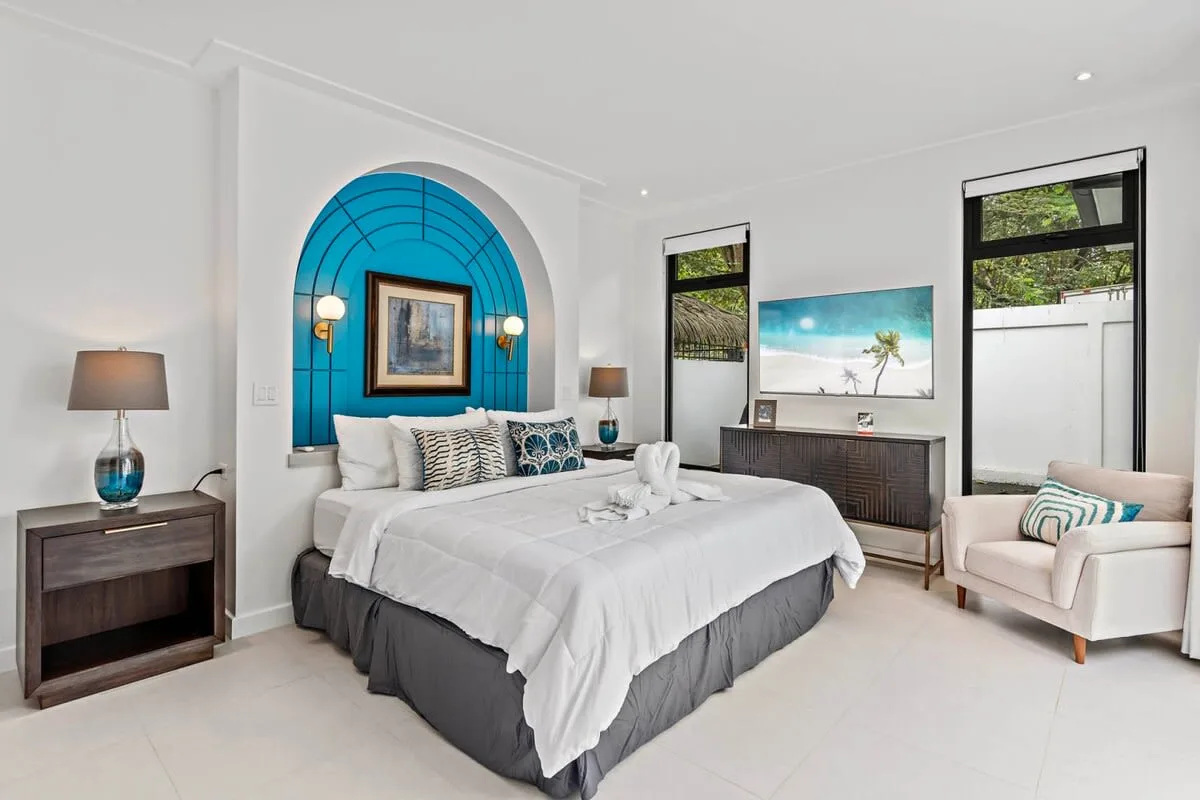 A bright bedroom features a large bed, blue arched wall detail, and a seating area.
