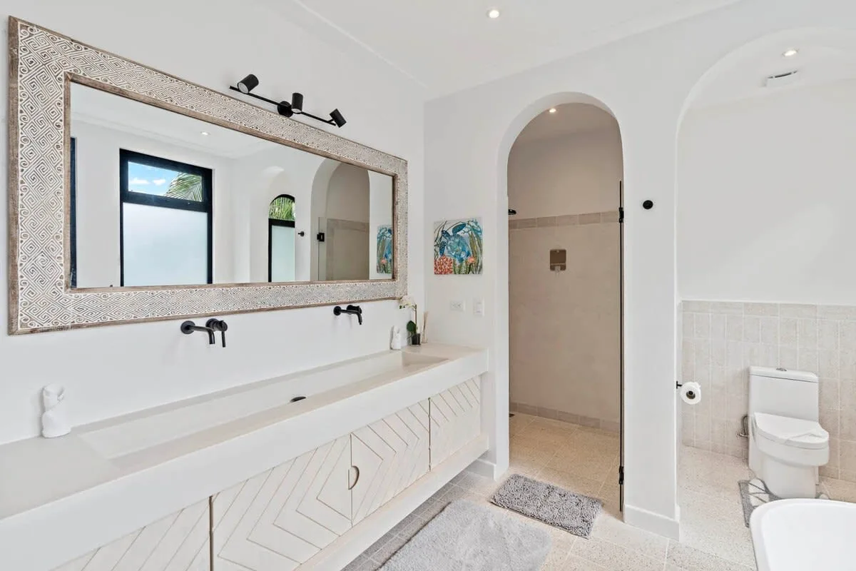 A bright bathroom with a long sink counter, large mirror, and arched shower entrance.
