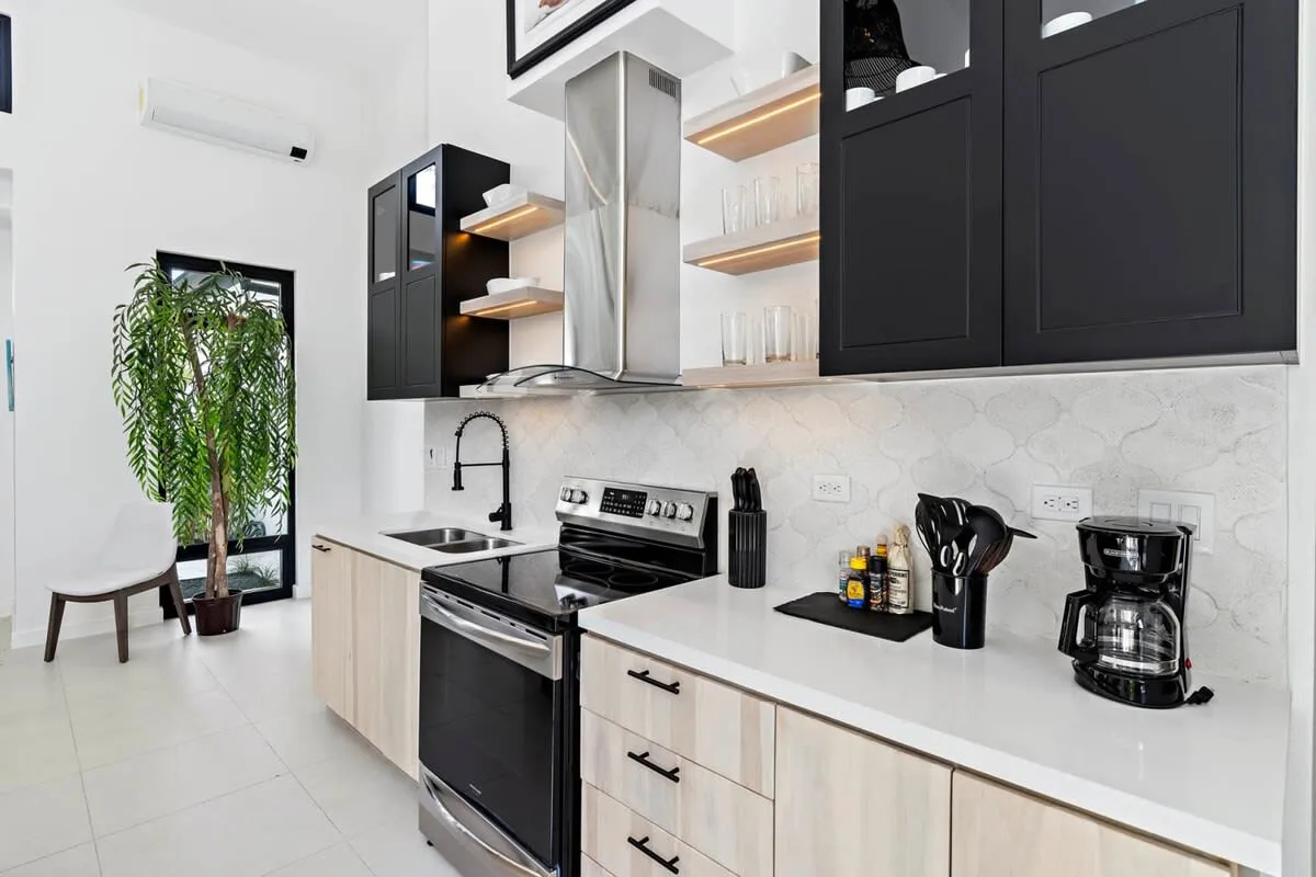 A bright kitchen with a stove, sink, and dark upper cabinets.